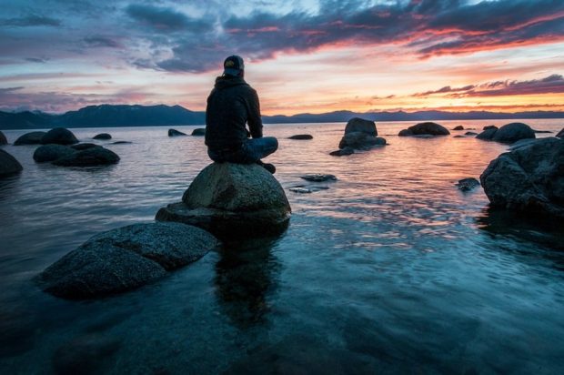 Modern Mystery School man on rock on sea shore